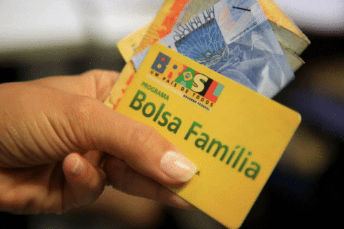 Cartão do programa Bolsa Família com dinheiro sendo segurado por uma pessoa, destacando o programa social do governo brasileiro.