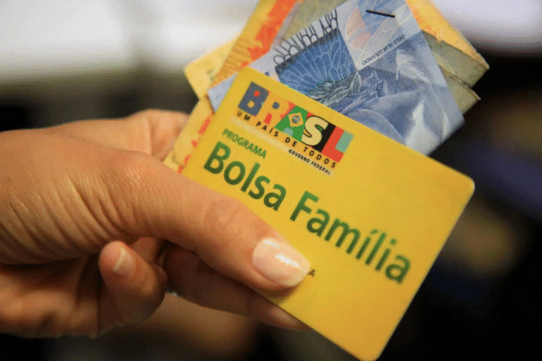 Cartão do programa Bolsa Família com dinheiro sendo segurado por uma pessoa, destacando o programa social do governo brasileiro.