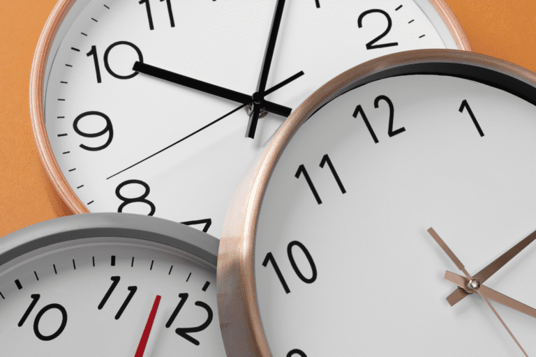 Três relógios analógicos sobrepostos, mostrando horários diferentes, em fundo laranja.