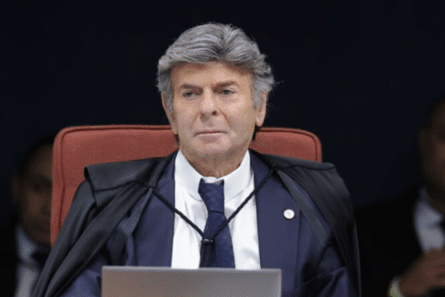 Fux, usando toga e gravata, com expressão séria, ao fundo uma audiência.