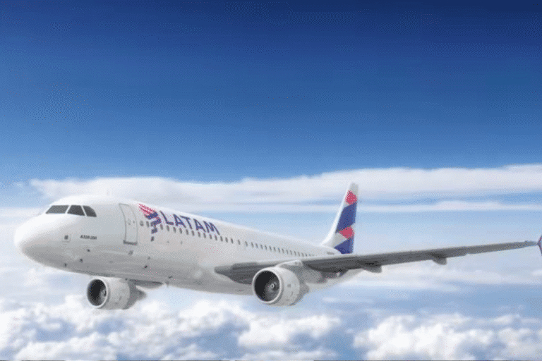 Um avião de passageiros com o logotipo da LATAM voa em um céu azul brilhante acima de nuvens brancas