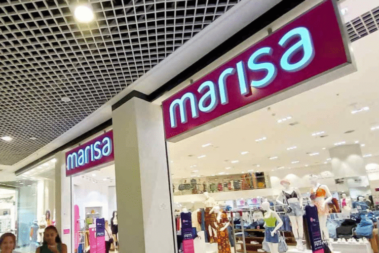 Fachada da loja Marisa no shopping, com o sinal iluminado em destaque e interior visível cheio de roupas e manequins.