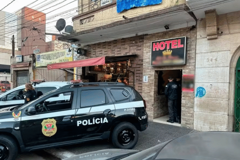 Polícia no entorno de um hotel, com viaturas e agentes em ação, na fachada de um estabelecimento em uma área urbana.