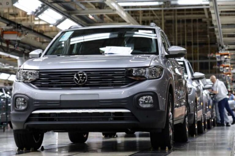 Linha de produção da Volkswagen com veículos cinza, funcionários trabalhando na montagem em fábrica automotiva.