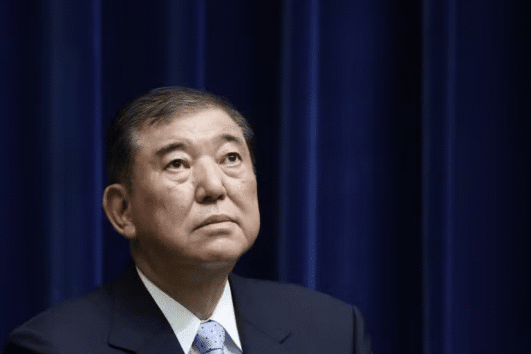 Imagem de um homem de terno escuro e gravata azul em frente a cortinas azuis, com expressão séria, representando liderança e confiança.