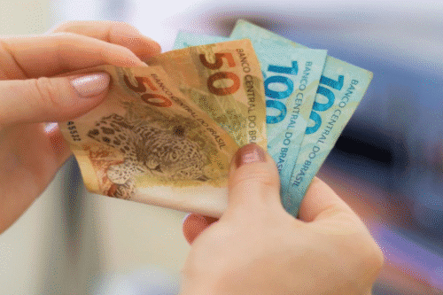 Pessoa trocando dinheiro brasileiro de cinquenta e dez reais, destaque para notas coloridas e detalhes das cédulas.