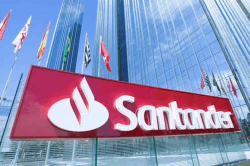 Fachada do banco Santander com marca visível em destaque, em frente a um prédio moderno de vidro, com várias bandeiras ao redor.