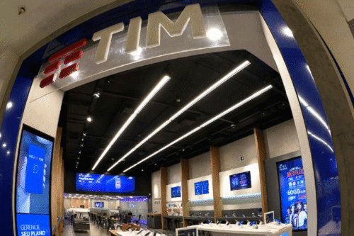 Interior de uma loja TIM com displays digitais, balcões de atendimento e ambiente moderno, focado em venda de planos e dispositivos móveis.