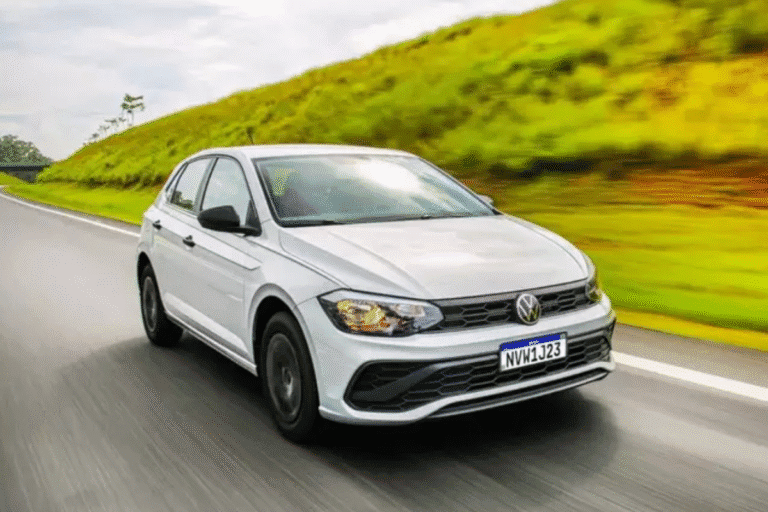 Imagem de um carro Volkswagen Voyage branco em movimento na estrada, com cenário verde ao fundo, destacando sua aparência moderna e economia de combustível.