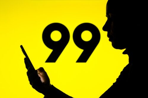 Silhueta com um celular na mão e o logo do 99 ao fundo