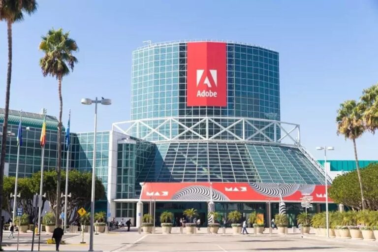 Centro de convenções na Los Angeles, com destaque para o logo da Adobe na fachada, rodeado por árvores e pessoas caminhando.