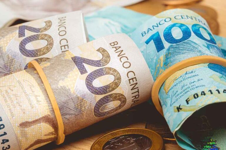 Notas de dinheiro brasileiro, incluindo cédulas de 200 e 100 reais, e moedas, sobre uma mesa de madeira, simbolizando economia e finanças no Brasil.