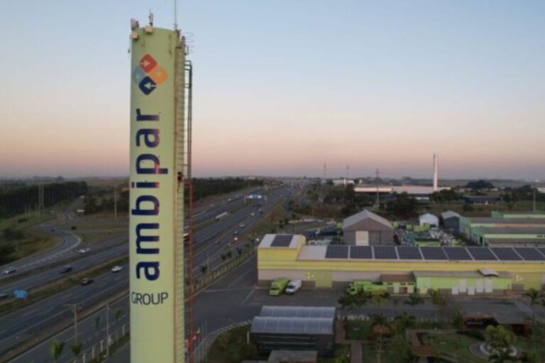 Torre de telecomunicações da Amplibar Group em uma cidade, com várias estradas e construções ao redor ao entardecer, céu claro e horizonte amplo.