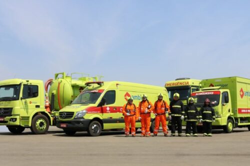 Imagem de veículos da Ambipar amparados por profissionais de resgate em uma pista, incluindo ambulância, caminhão de emergência e bombeiros.