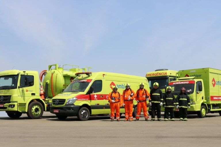 Imagem de veículos da Ambipar amparados por profissionais de resgate em uma pista, incluindo ambulância, caminhão de emergência e bombeiros.