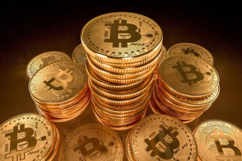 Imagem de várias moedas de bitcoin douradas empilhadas, destacando a valorização e o interesse na criptomoeda Bitcoin, símbolo do mercado de criptomoedas.