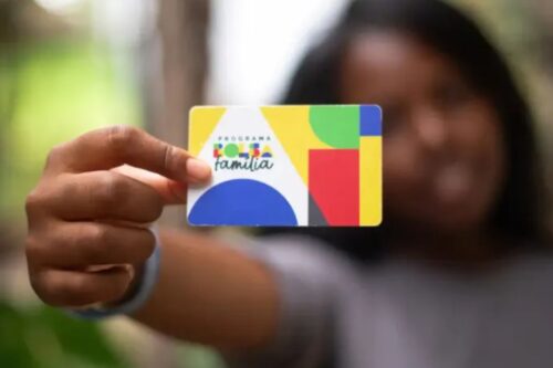Pessoa segurando um cartão do programa Bolsa Família, com fundo desfocado, promovendo assistência social no Brasil.