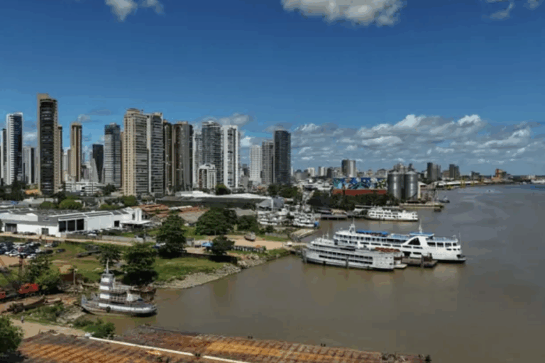 Paisagem urbana de Belém com arranha-céus altos ao lado de um rio, com vários barcos atracados, sob céu azul com nuvens, em uma cidade cosmopolita.