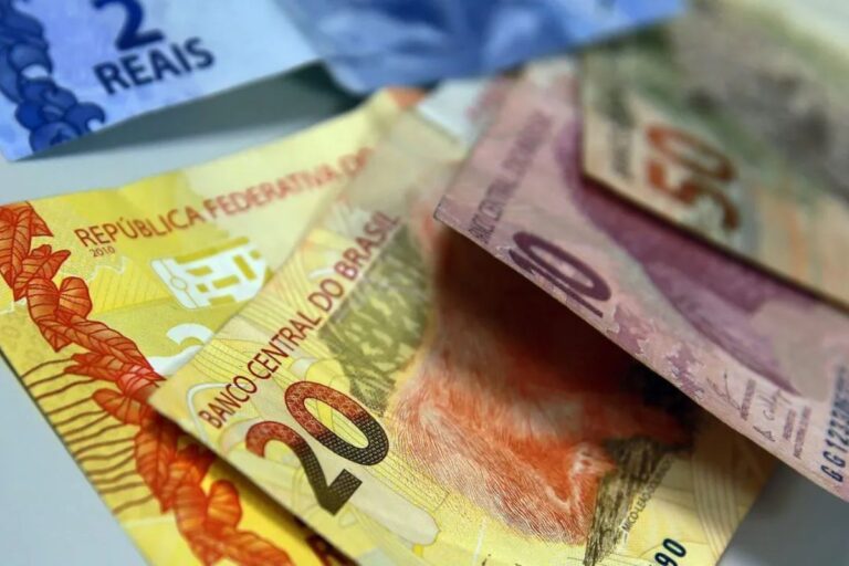 Imagem de notas de dinheiro brasileira de diferentes valores, incluindo notas de 2, 10 e 20 reais, espalhadas sobre uma superfície.