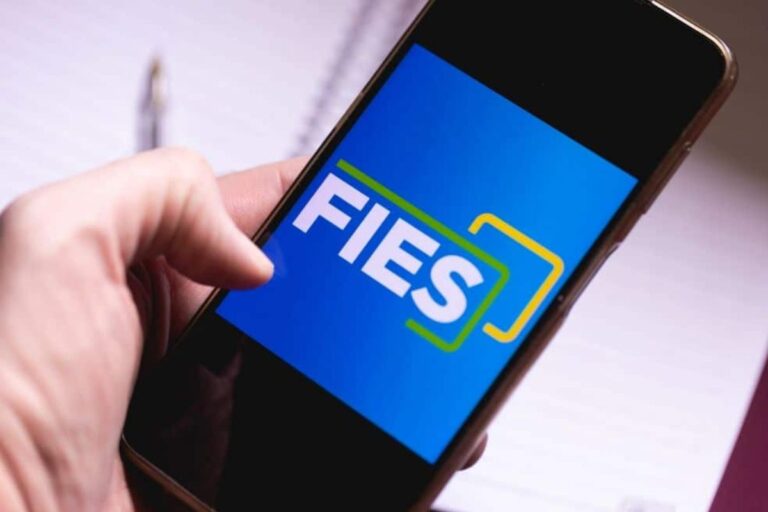 Pessoa segurando um celular exibindo a tela do aplicativo de declaração de imposto de renda FIES, foco na tela com logo em destaque.
