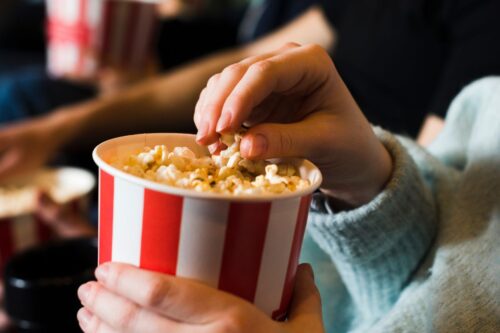 Pessoa segurando balde de pipoca, desfrutando de um momento de lazer em um cinema ou evento, com foco na pipoca de cinema.