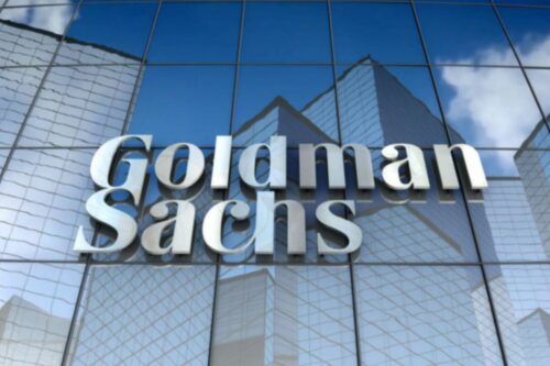 Fachada de um edifício moderno com o logotipo da Goldman Sachs em destaque na frente de vidro refletor, simbolizando finanças e investimentos.
