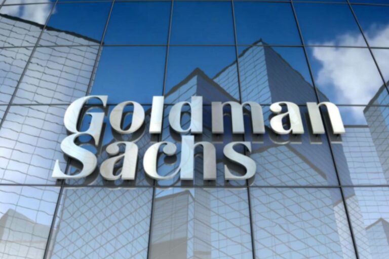 Fachada de um edifício moderno com o logotipo da Goldman Sachs em destaque na frente de vidro refletor, simbolizando finanças e investimentos.