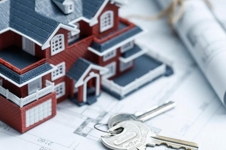 Maquete de uma casa de design detalhado, com chaves de metal no primeiro plano, simulando planejamento e financiamento imobiliário, sobre um projeto arquitetônico.