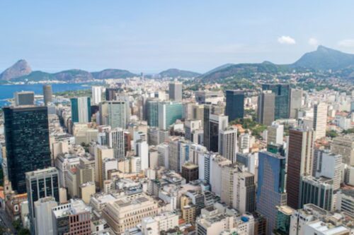 Vista panorâmica do centro financeiro do Rio de Janeiro com arranha-céus, a Baía de Guanabara ao fundo e o Cristo Redentor ao longe, capturando a beleza urbana e natural da cidade.