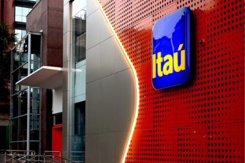 Edifício moderno com fachada de vidro e sinalização do banco Itaú em destaque na rua, com iluminação atraente e arquitetura contemporânea.