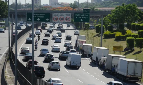 Foto mostra a Linha Amarela, via expressa que liga a Ilha do Fundão à Barra da Tijuca, no Rio de Janeiro, com intenso fluxo de veículos sob céu claro.