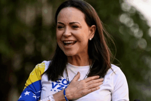 Maria Corina, vencedora do Nobel da paz, sorridente em movimento ao ar livre, usando camiseta branca com detalhes em azul e amarelo, com uma expressão de alegria e entusiasmo.