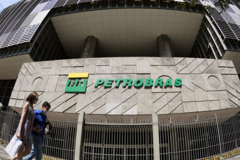 Imagem da sede da Petrobras com logo verde e pessoas caminhando na frente do prédio em horário diurno