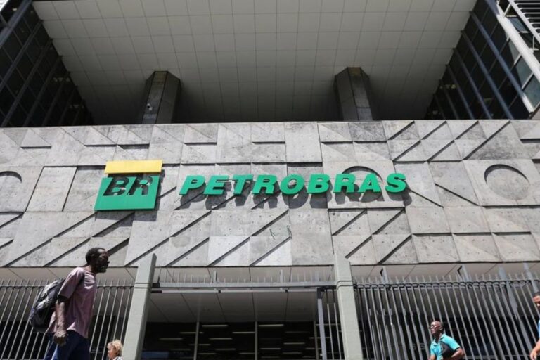 Fachada do edifício da Petrobras com logo em destaque, com pessoas caminhando na frente em um dia ensolarado.