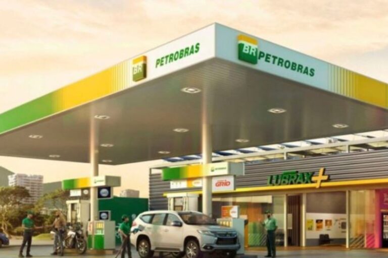 Imagem de um posto de gasolina Petrobras com clientes abastecendo seus veículos e funcionários atendendo na loja de conveniência, em um dia ensolarado.