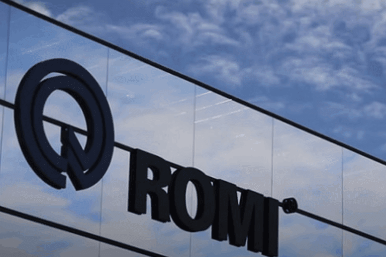 Imagem de um edifício com fachada de vidro refletindo o céu e as nuvens, destacando a logomarca da Romi (ROMI3)