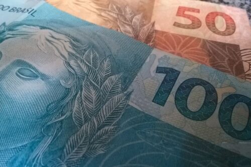 Imagem de notas de dinheiro brasileiro, incluindo cédulas de 50 e 100 reais, simbolizando o salário mínimo