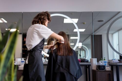 Cabeleireira cortando cabelo de uma cliente em salão de beleza moderno e iluminado, com espelhos grandes e decoração elegante.