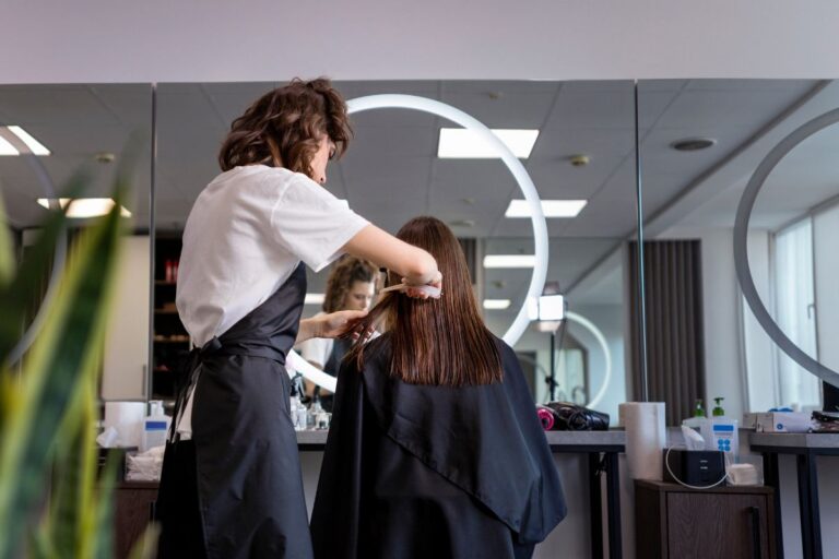 Cabeleireira cortando cabelo de uma cliente em salão de beleza moderno e iluminado, com espelhos grandes e decoração elegante.
