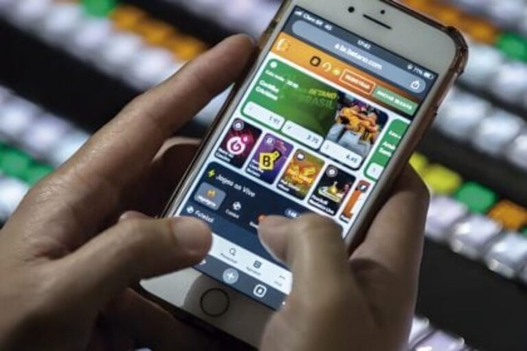 Pessoa usando um smartphone para acessar um aplicativo de jogos e apostas online, com várias opções de jogos na tela.