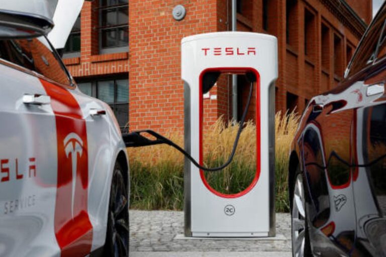 Carros elétricos Tesla conectados à estação de carregamento em frente a um prédio de tijolos, evidenciando infraestrutura de veículos elétricos moderna.