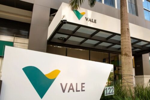 Fachada de um prédio empresarial com logo da Vale, empresa de mineração, e uma placa grande com o nome Vale ao lado de uma palmeira