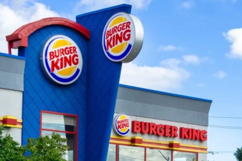 Fachada de uma loja Burger King com o logo visível e céu azul ao fundo, destacando-se pelo ambiente moderno e convidativo.