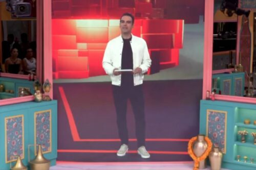 Tadeu Schmidt apresentando BBB 26 no estúdio com decoração colorida e público ao fundo, promovendo entretenimento na TV brasileira.