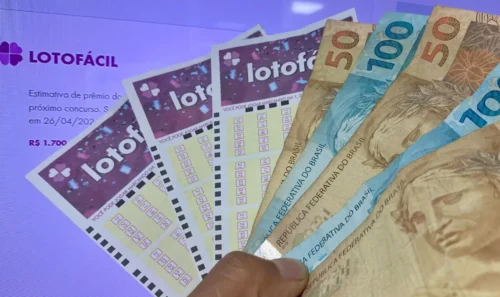 Notas de real e volantes da Lotofácil exibidos em frente a uma tela com informações sobre o prêmio do próximo concurso da Loteria Caixa - Lotofacil 3514