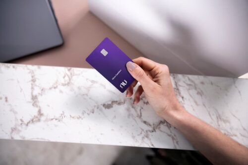 Pessoa segura um cartão roxo do Nubank Ultravioleta sobre uma mesa de mármore, associado a benefícios de sala VIP.