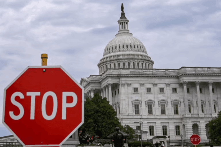 Placa de trânsito com a palavra STOP em frente ao prédio do Capitólio dos Estados Unidos em Washington, simbolizando a paralisação do governo (shutdown).