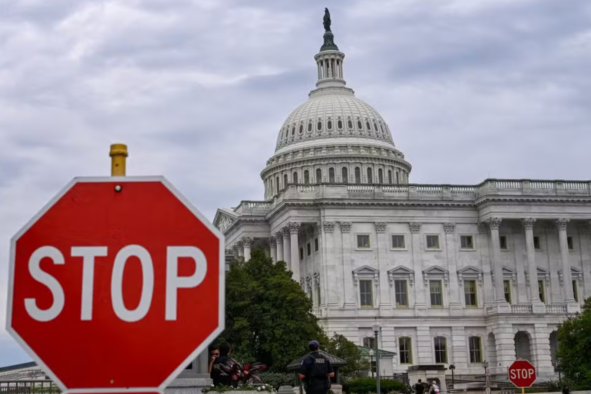 Placa de trânsito com a palavra STOP em frente ao prédio do Capitólio dos Estados Unidos em Washington, simbolizando a paralisação do governo (shutdown).