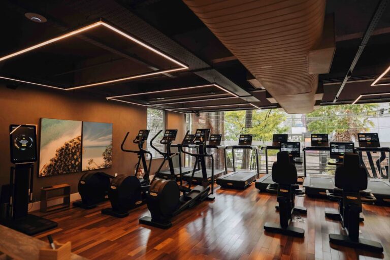 Sala de treinos moderna da SIX Sport Life com esteiras, bicicletas e design sofisticado em madeira.
