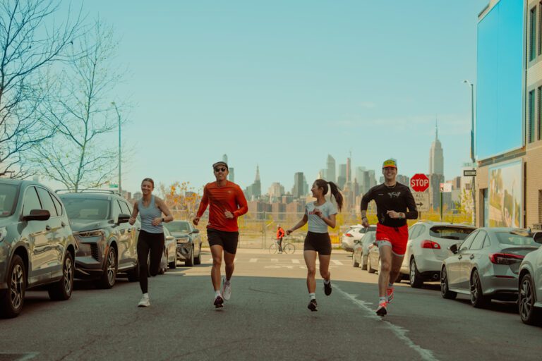 Quatro pessoas correm juntas em uma rua urbana com vista para os prédios de Nova York ao fundo, representando o espírito comunitário e ativo promovido pelo aplicativo Strava.